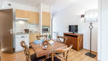 A compact kitchen with wooden cabinets, a microwave, and a dining area with a wooden table and chairs.