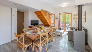 A dining area with a wooden table and chairs, a TV, and a staircase leading to a balcony.