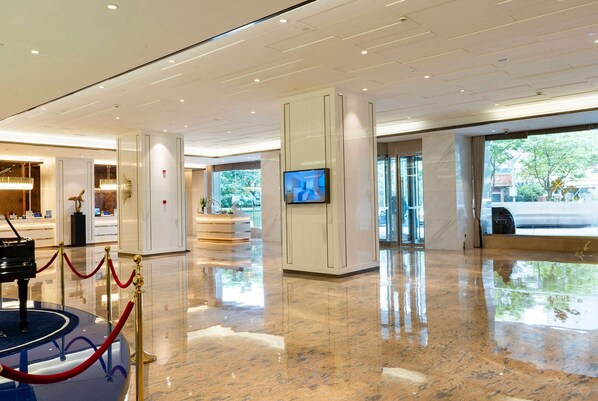 A spacious lobby with a grand piano, a television screen, and a red rope barrier. - Howard Johnson Wyndham Leonora plzaz Shanghai (Shanghai)