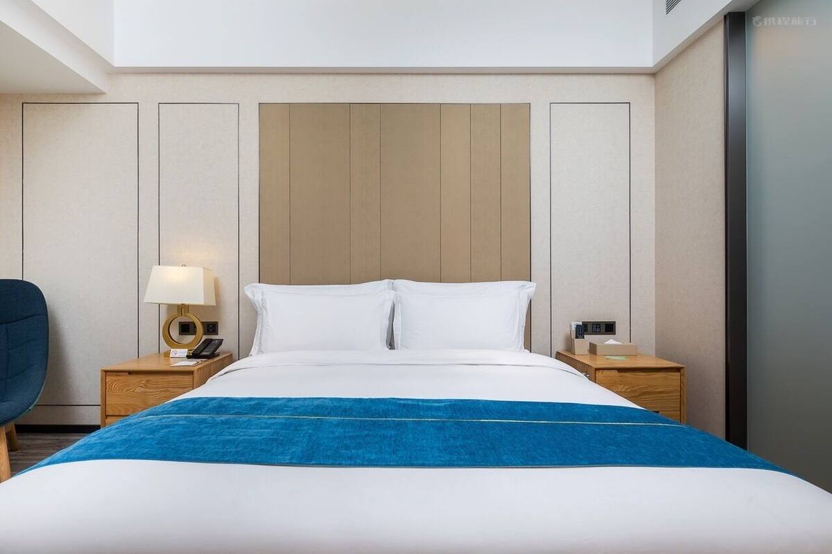A hotel room with a bed, two bedside tables, a lamp, a chair, and a wooden headboard.