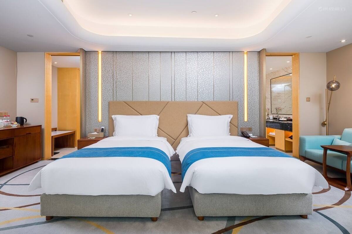 A hotel room with two beds, a desk, a chair, a mirror, and a bathroom.