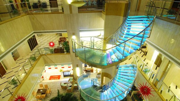 A multi-level atrium with a glass-walled spiral staircase, seating areas, and indoor plants. - Howard Johnson Wyndham Leonora plzaz Shanghai (Shanghai)