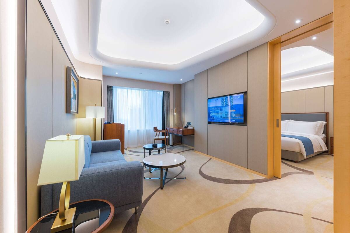A modern hotel room with a sofa, a desk, a TV, and a bed.