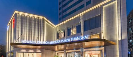 The exterior of Howard Johnson Leonora Plaza Shanghai with a modern design, featuring a prominent entrance and illuminated signage.