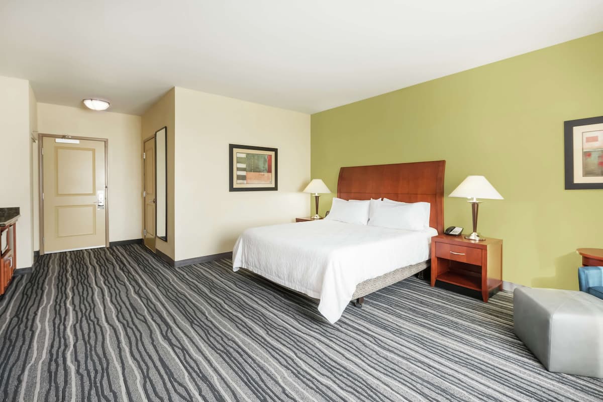 A hotel room with a bed, bedside lamps, a nightstand, a chair, and a door.