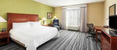 A hotel room with a large bed, two bedside tables with lamps, a desk with a chair, a television, and a window with curtains.