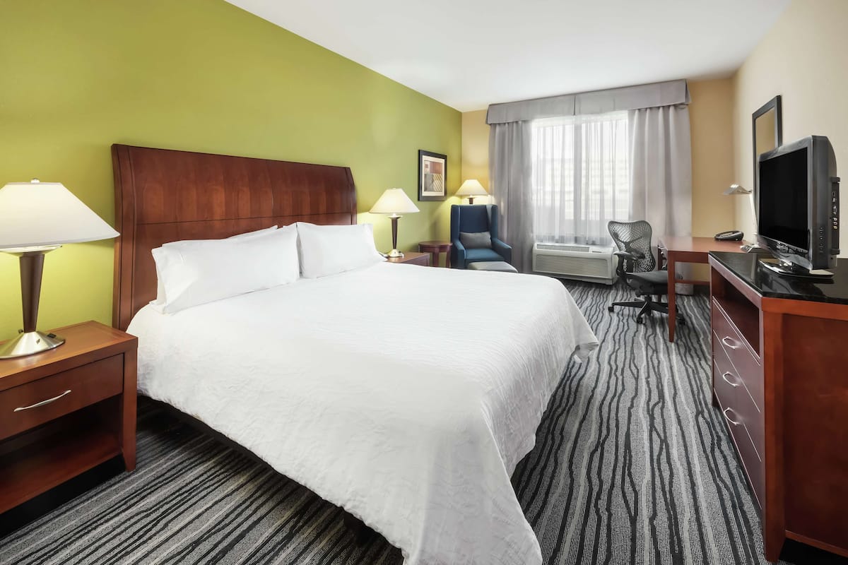 A hotel room with a large bed, a desk with a computer, a chair, and a TV.