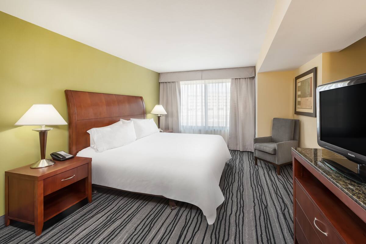 A hotel room with a bed, nightstand, TV, and a chair.