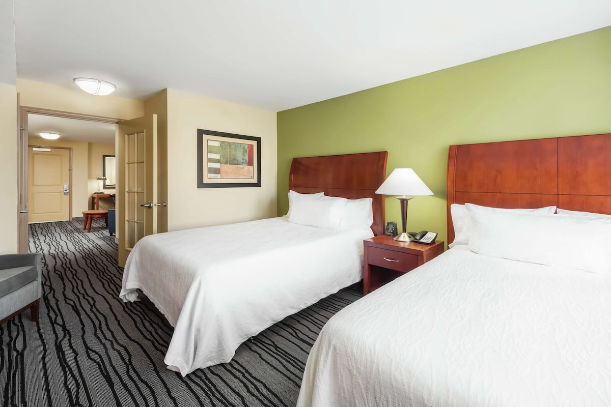 A hotel room with two beds, a desk, a chair, and a painting on the wall.