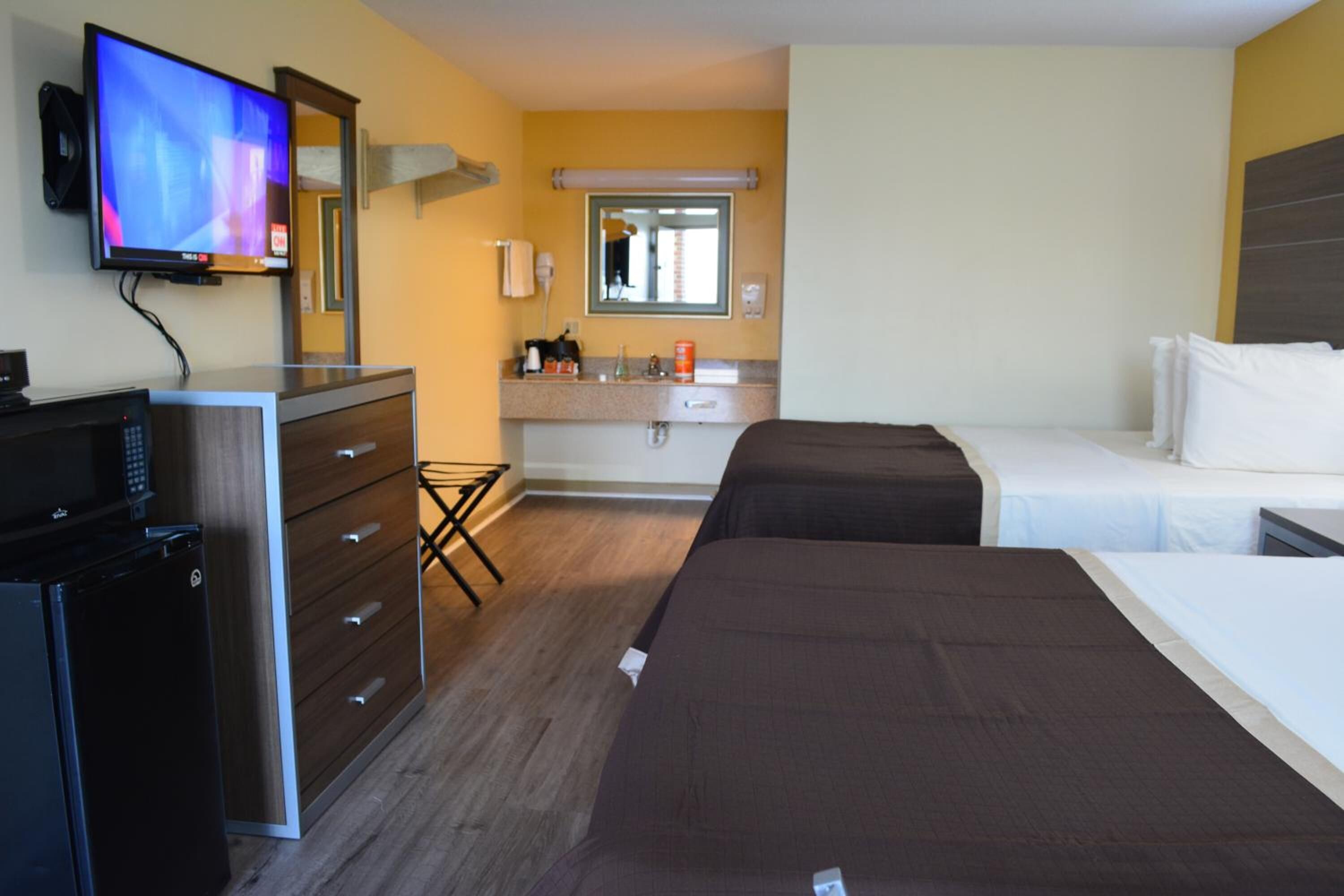 A hotel room with a TV, a minibar, a desk, a bed, a bedside table, and a bathroom with a mirror and sink.