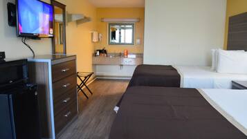 A hotel room with a TV, a minibar, a desk, a bed, a bedside table, and a bathroom with a mirror and sink.