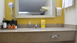 A bathroom with a granite countertop, a sink, a hair dryer, a bottle of wipes, and a soap dispenser. - Southern Inn Lumberton (Lumberton)