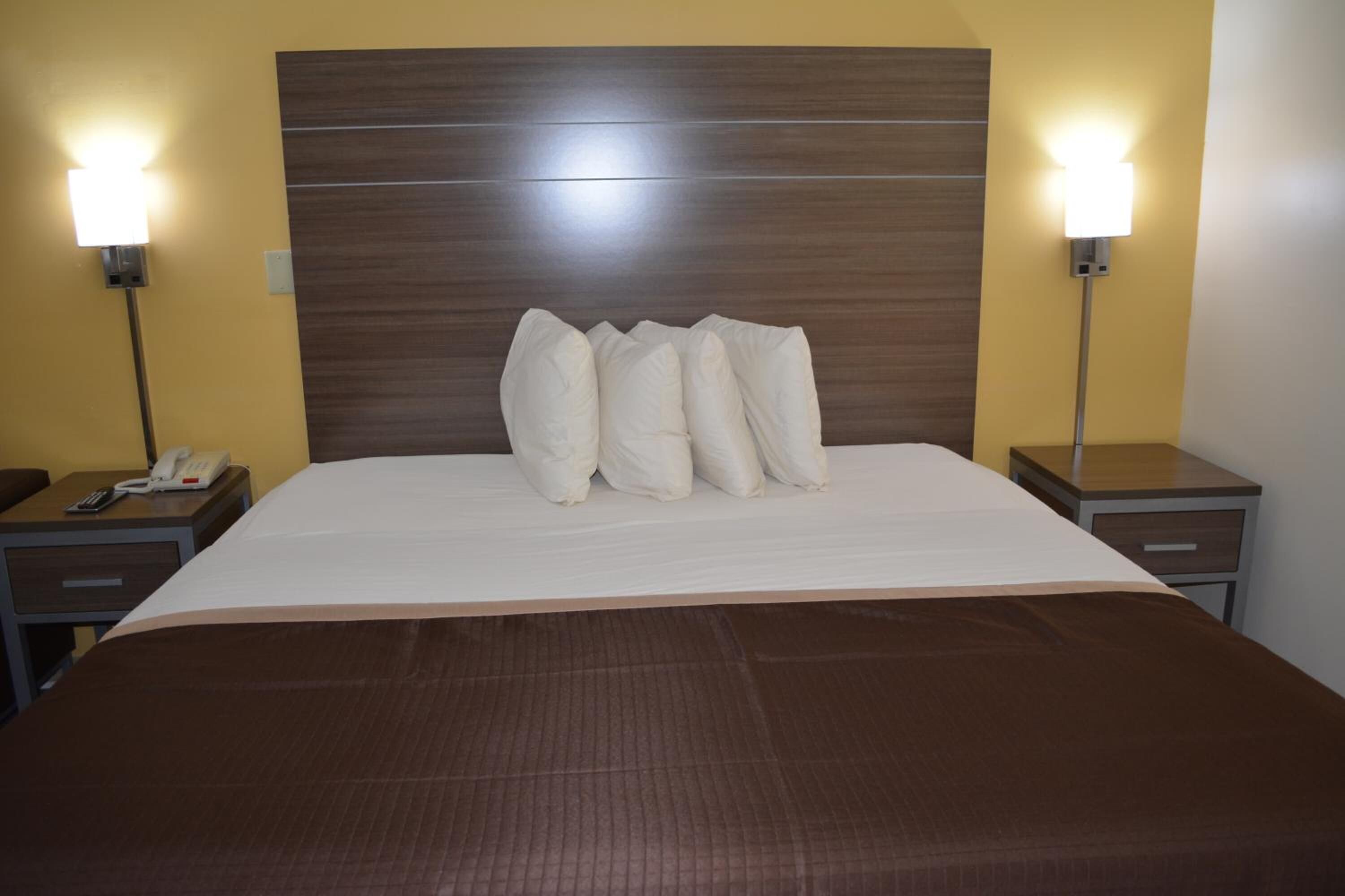 Une chambre d’hôtel avec un grand lit, deux tables de chevet, une petite table et deux lampes fixées au mur.