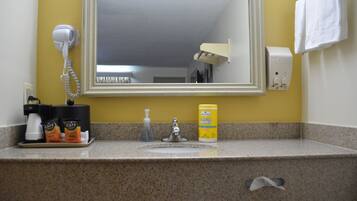 Un baño con lavamanos, secador de pelo, jabón de manos en botella y recipientes con toallitas.