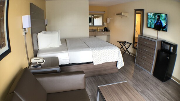 A hotel room with a bed, a desk, a chair, a dresser, a television, and a small table. - Southern Inn Lumberton (Lumberton)