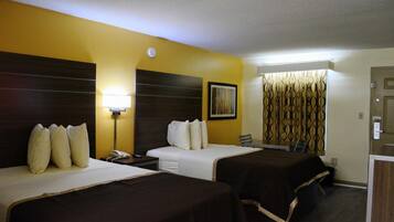 Habitación de hotel con dos camas, una mesita de noche, una lámpara, un cuadro y una cortina estampada.