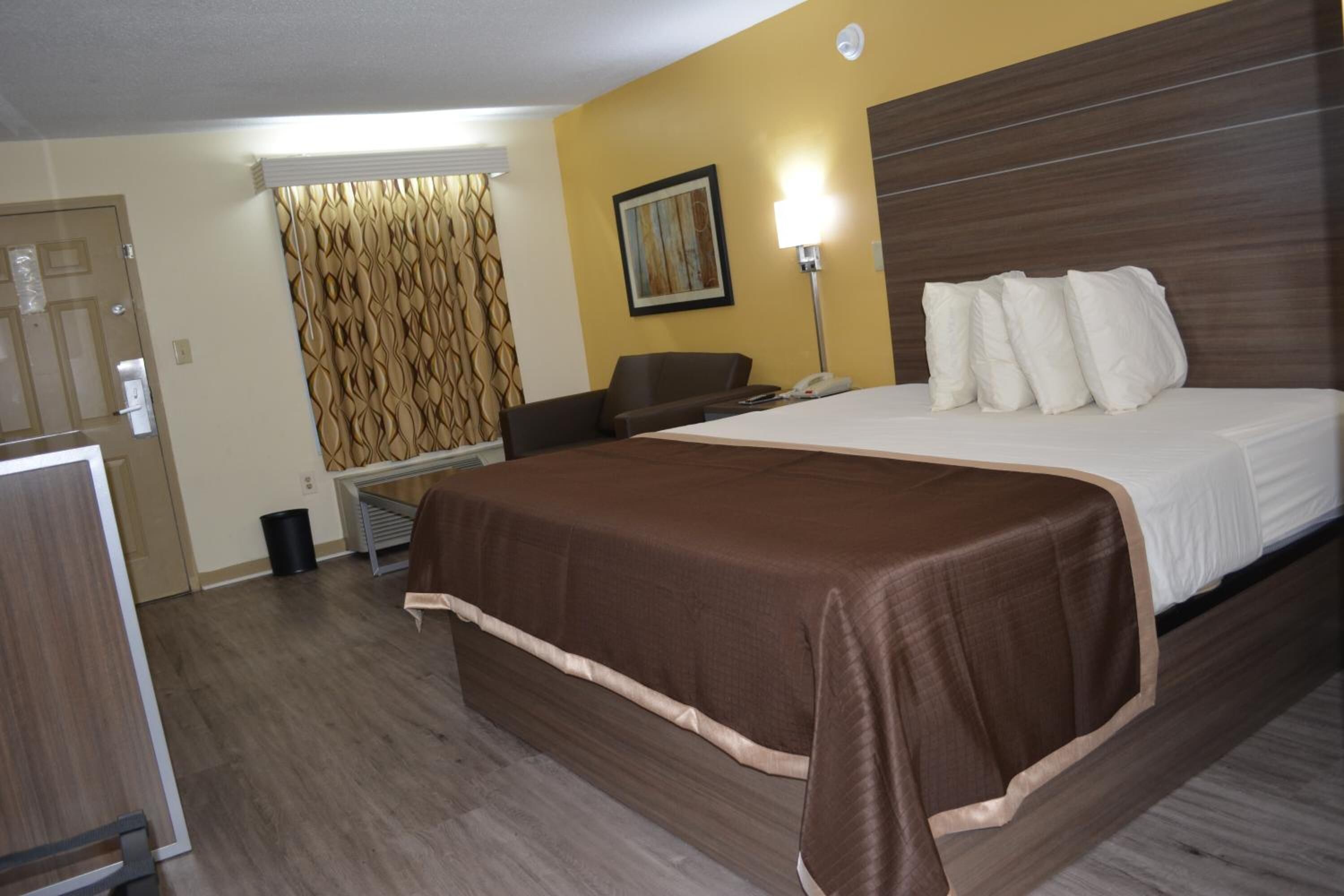 A hotel room with a large bed, a desk, a chair, a lamp, and a painting on the wall.