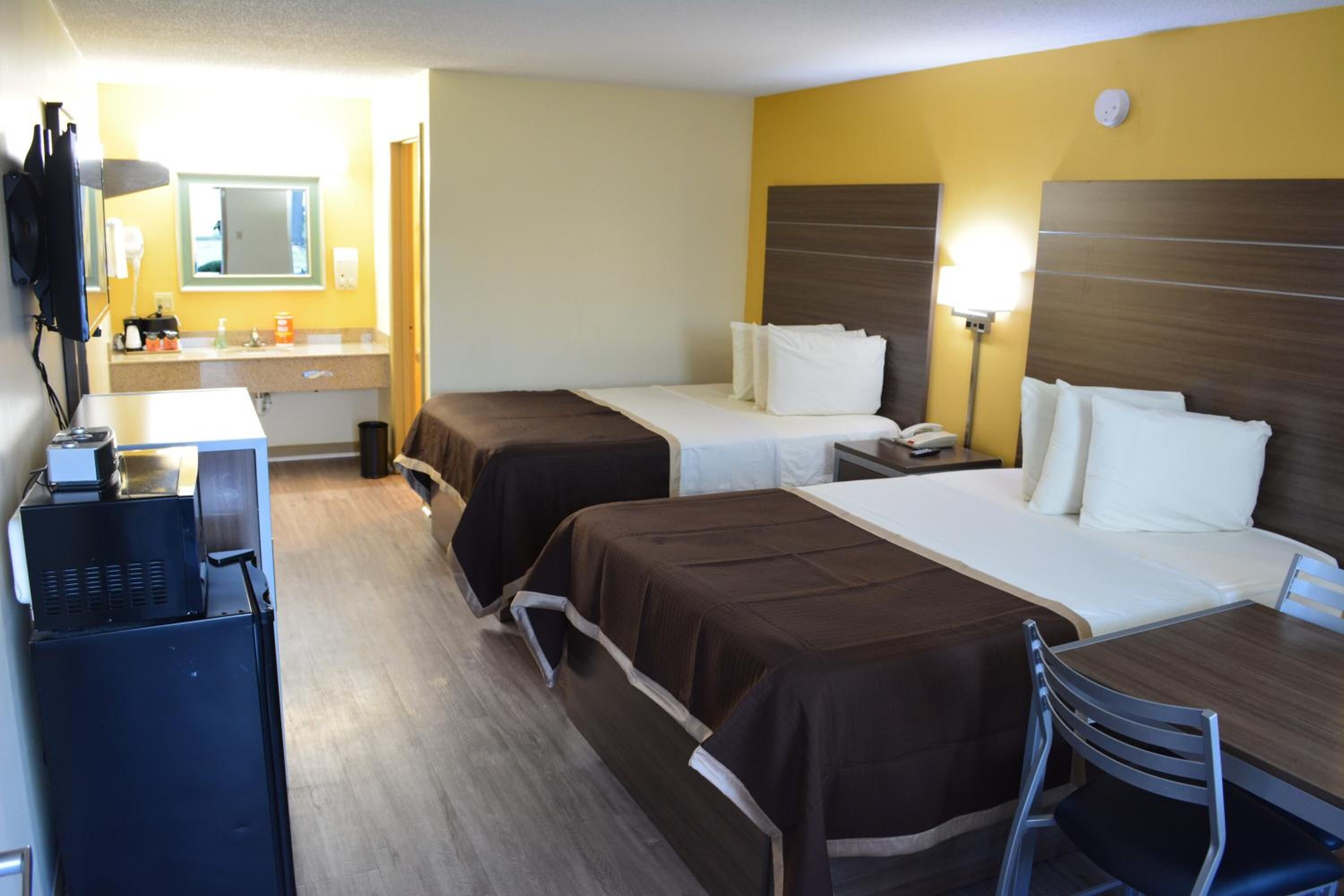 A hotel room with two beds, a desk, a chair, a small table, a mirror, and a television.