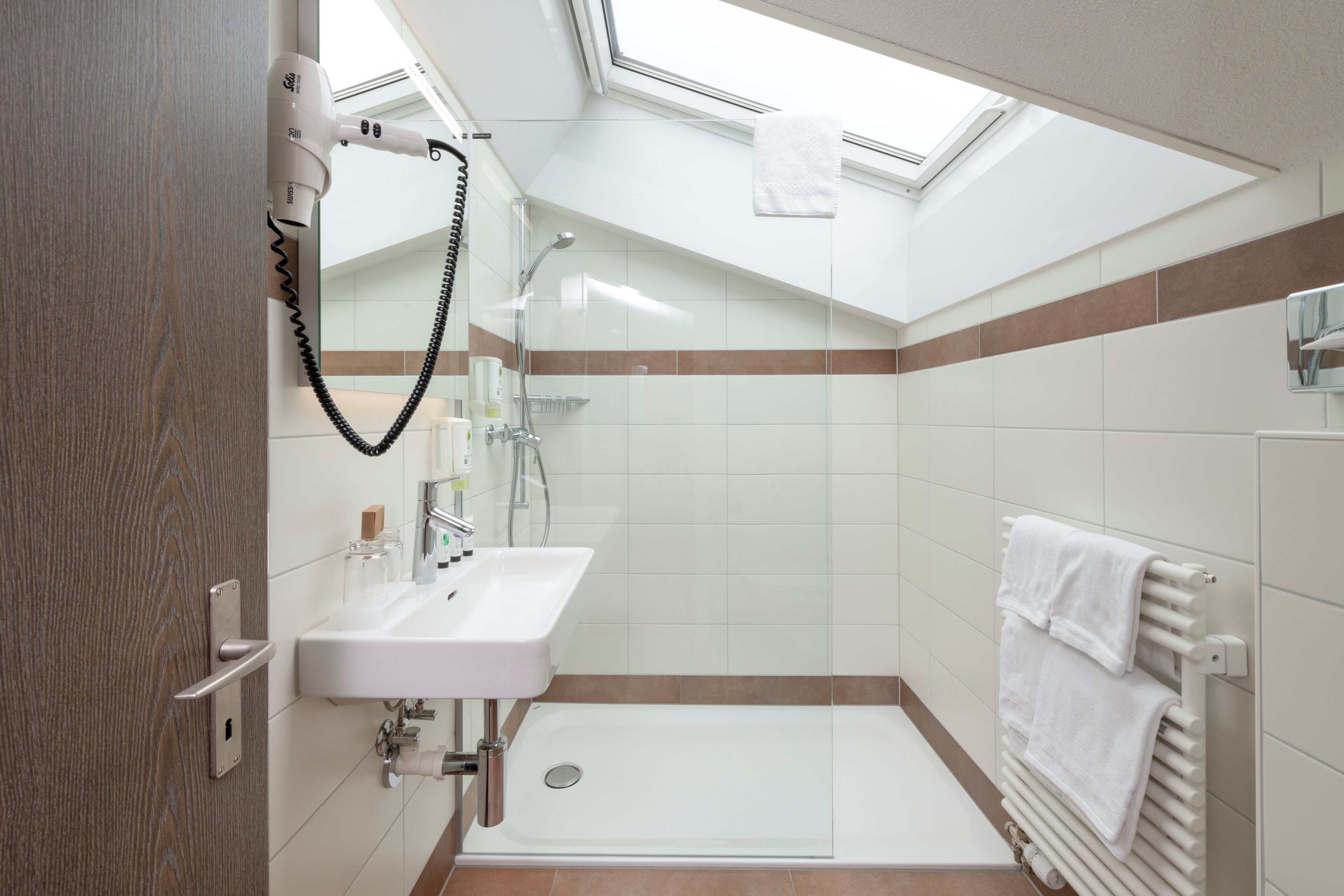 A modern bathroom with a skylight, a shower, a sink, and a towel rack.