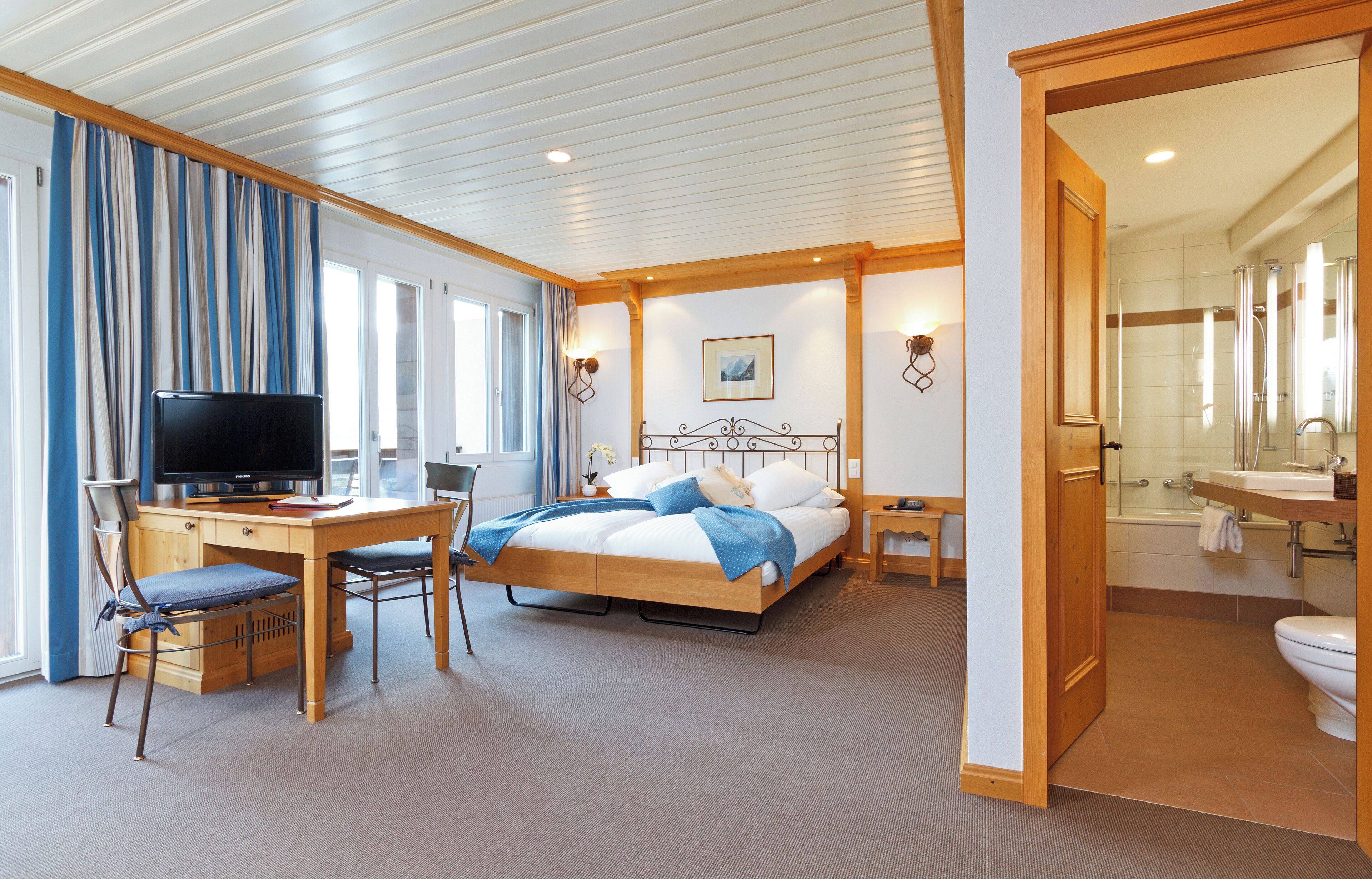 A hotel room with a bed, desk, chair, television, and a bathroom.