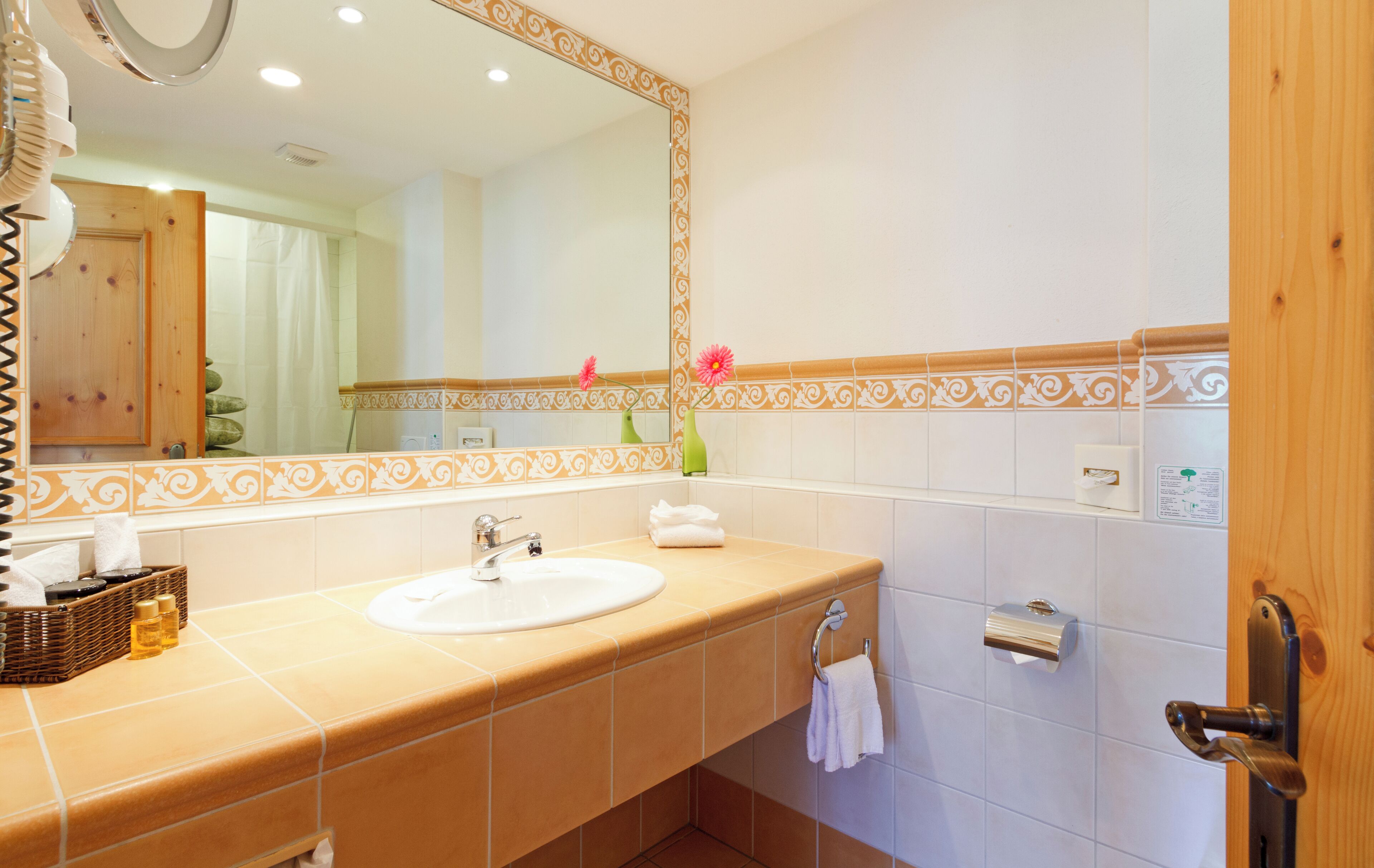 A bathroom with a beige sink, a large mirror, and a wooden door.