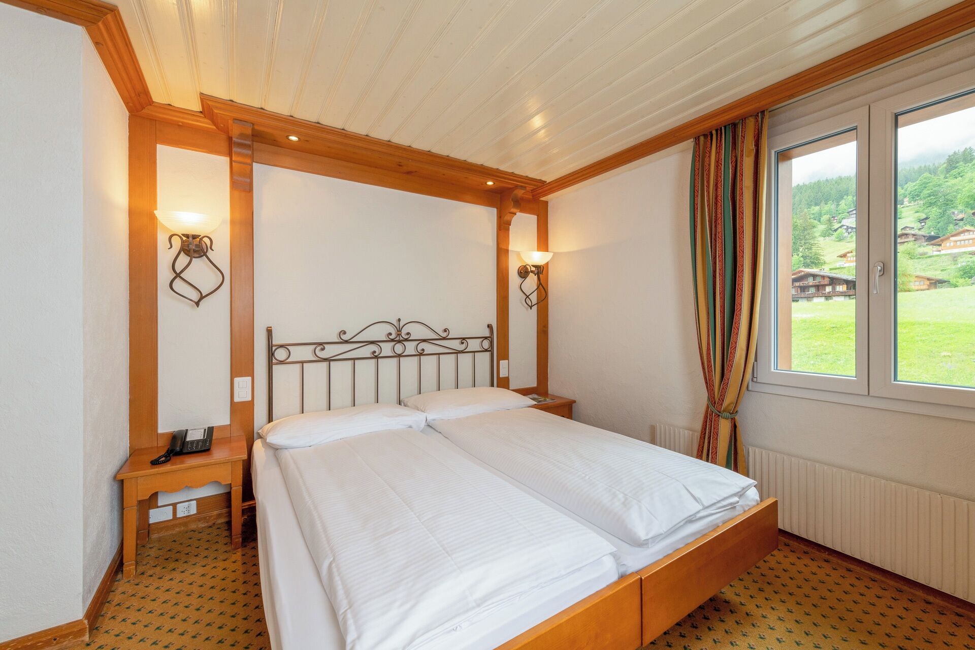 A double bed with a wooden headboard, two bedside tables, and a window with curtains.