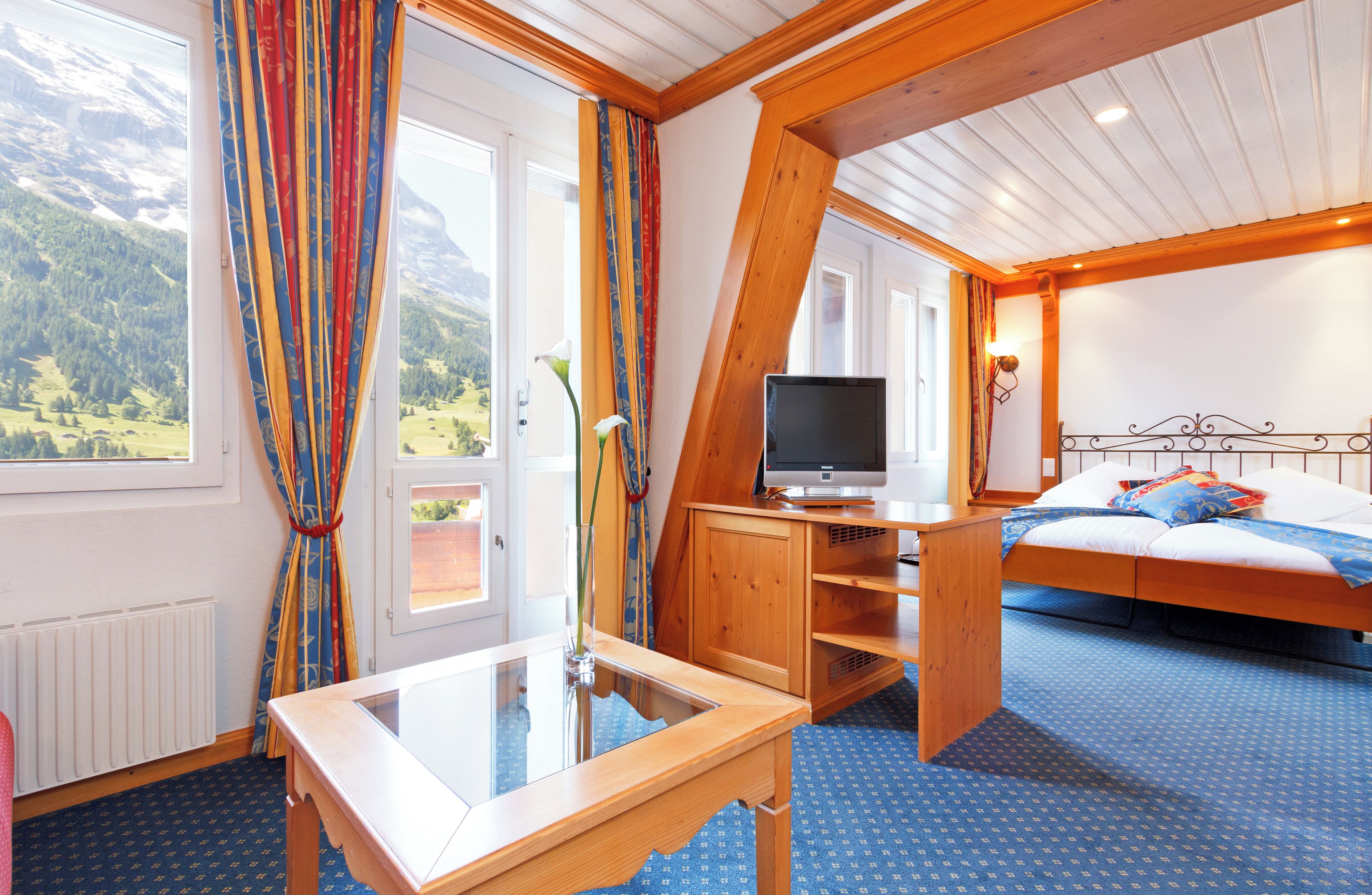 Una habitación con una cama, televisión, escritorio de madera y ventana con cortinas.