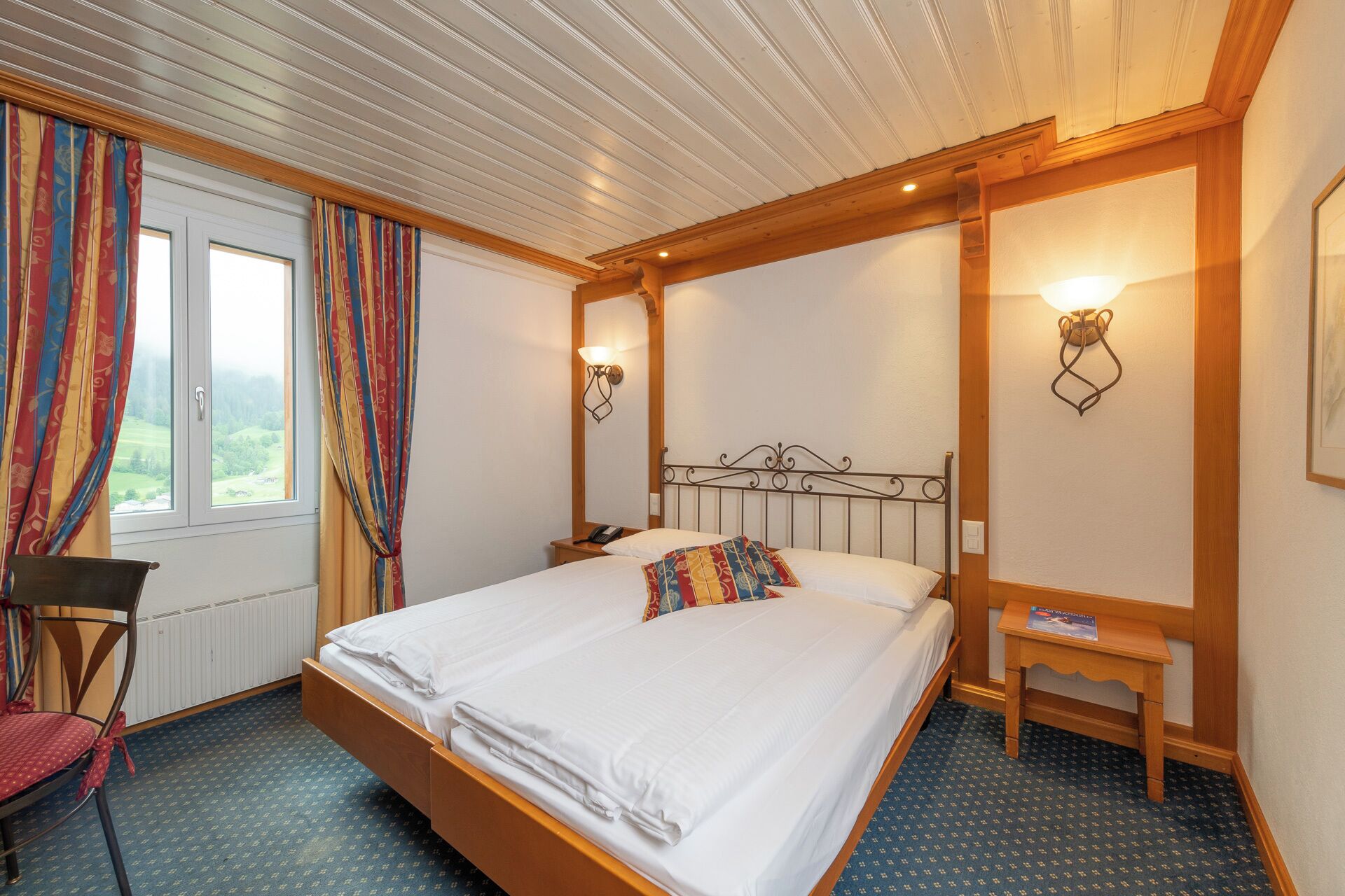 Une chambre d’hôtel avec un grand lit, une chaise, une table de chevet et une fenêtre avec des rideaux.