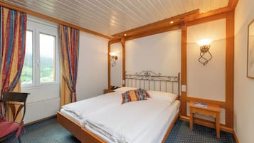 Una habitación de hotel con una cama grande, una silla, una mesita de noche y un ventanal con cortinas.