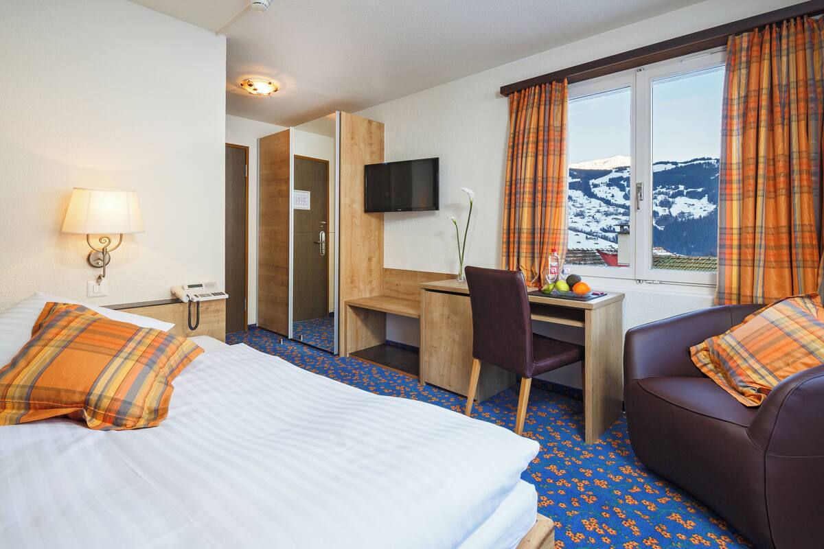 Ein Hotelzimmer mit zwei Betten, einem Schreibtisch, einem Stuhl, einem Fernseher und einem Fenster mit Vorhängen.