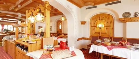 A dining area with wooden tables, white tablecloths, and red patterned placemats. There are various food items and glassware on the tables.