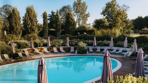 A swimming pool with lounge chairs and umbrellas, surrounded by greenery and trees. - Albergo dell'Agenzia (Bra)