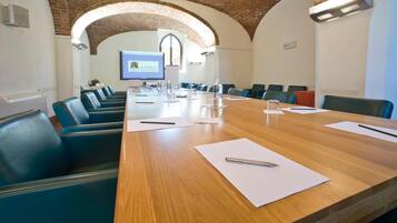 Una sala conferenze con un lungo tavolo di legno, sedie blu e uno schermo proiettore che mostra un logo.