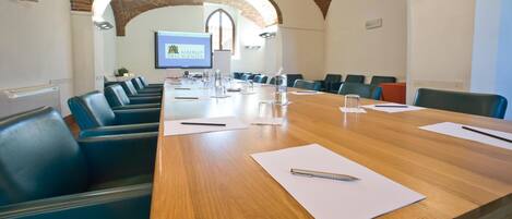 A conference room with a long wooden table, blue chairs, and a projector screen displaying a logo.