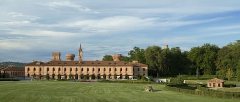 A large, historic building with multiple towers and arched windows, surrounded by well-maintained gardens and a clear sky.