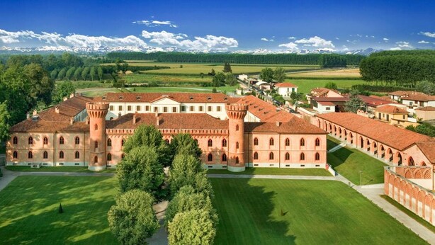 A large, historic building with a central courtyard, surrounded by lush greenery and a mountainous backdrop. - Albergo dell'Agenzia (Bra)