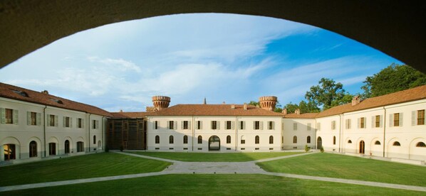 A courtyard with a central building featuring arched windows and a tiled roof, surrounded by a well-maintained lawn. - Albergo dell'Agenzia (Bra)