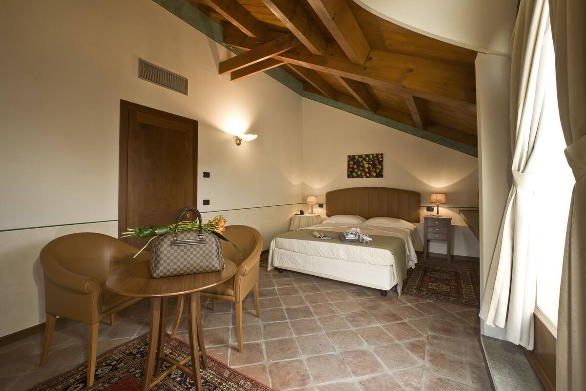 A hotel room with a bed, bedside table, chair, and a small table with a handbag.