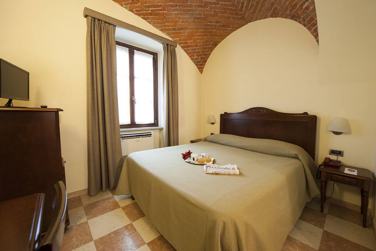 A hotel room with a bed, a desk, a television, and a window with curtains.