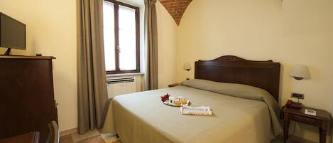 A hotel room with a bed, a desk, a television, and a window with curtains.