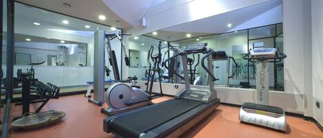 Academia moderna com diversos equipamentos de exercício, incluindo esteiras e máquinas de peso, e grandes espelhos nas paredes.
