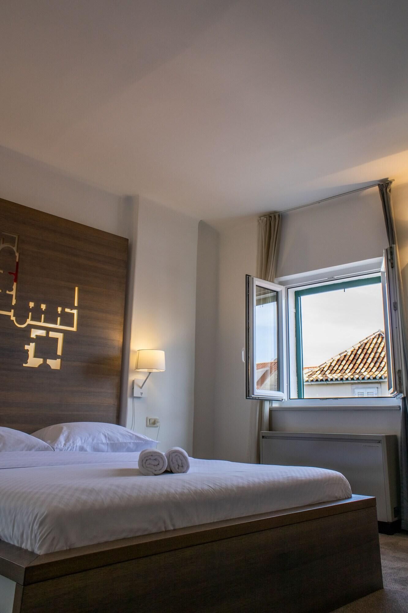 A hotel room with a bed, a wall-mounted map, a window with curtains, and a radiator.