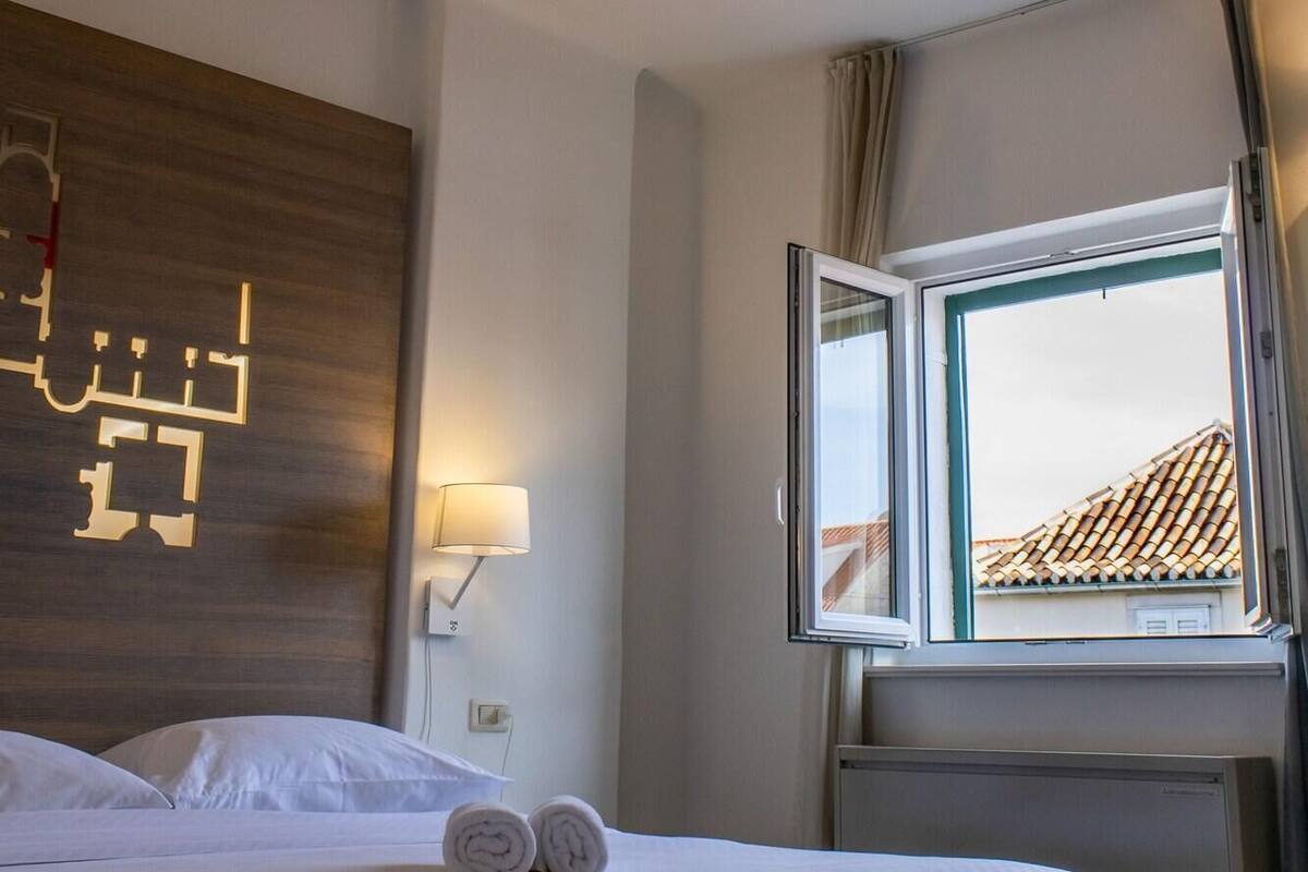 Une chambre d’hôtel avec un lit, une carte accrochée au mur, une fenêtre avec des rideaux et un radiateur.