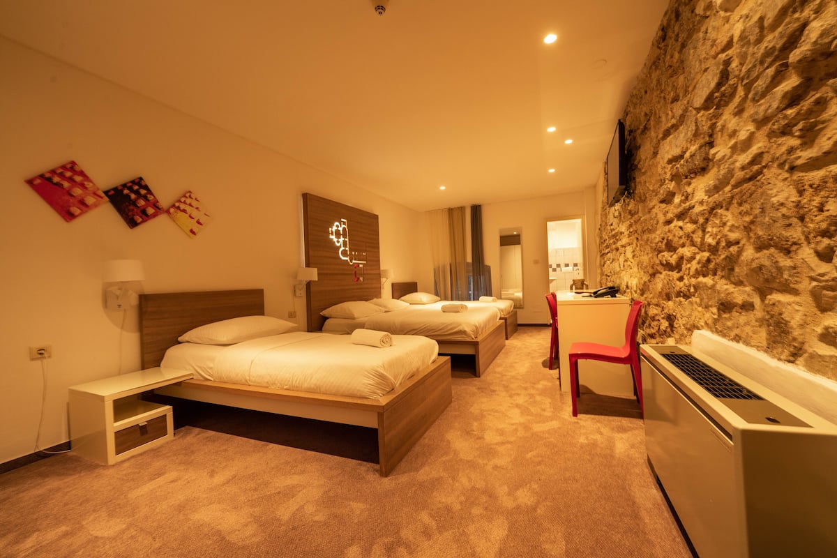 Ein Hotelzimmer mit drei Betten, einem Schreibtisch, einem Stuhl und einer Steinwand.