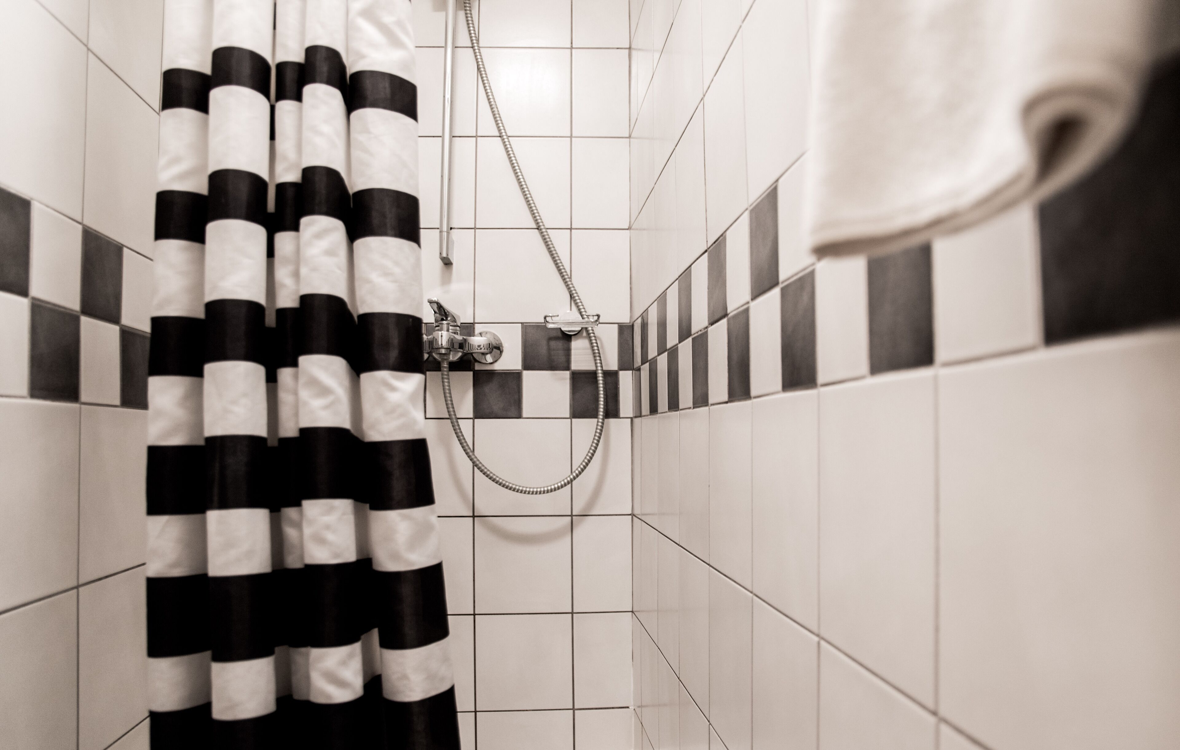 A bathroom with a black and white striped shower curtain, a towel hanging on the wall, and a tiled floor.