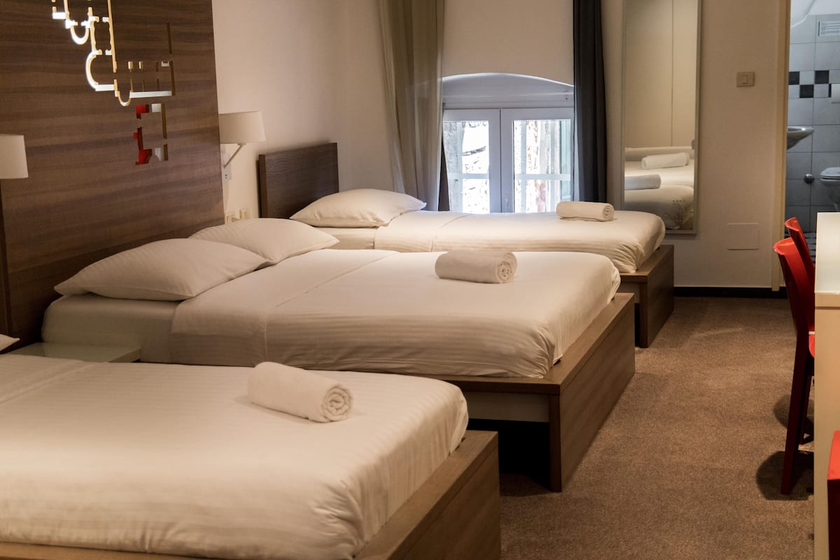 Ein Hotelzimmer mit drei Betten, einem Holzkopfstück, einem großen Spiegel und Blick nach draußen.