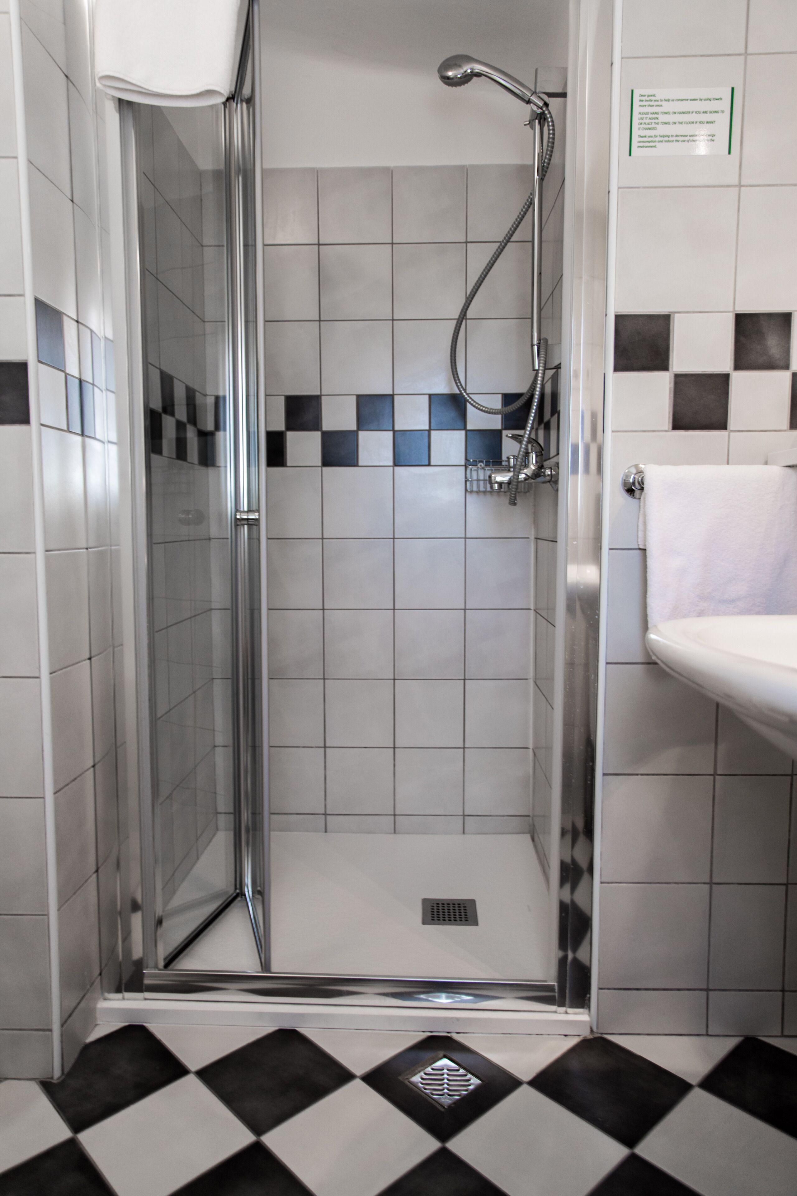 A shower area with a glass door, a white sink, and a tiled floor with a black and white pattern.