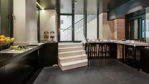 A modern kitchen with a central staircase, a dining area with a long table, and a view of the outside through large windows. - Slavija Culture Heritage Hotel (Split)