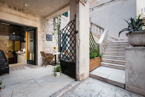 Step into a charming courtyard with a rustic charm, featuring a stone floor, wooden bench, and an entrance.