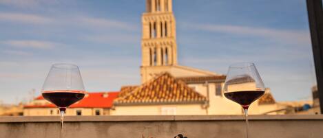 Two wine glasses on a table with a plate of food and a view of a tower in the background.